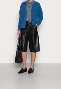 Blå fluffig cardigan, grå skjorta med knappar, svarta lädershorts, svarta loafers och en svart tote-väska. Släta texturer och kontrasterande färger.