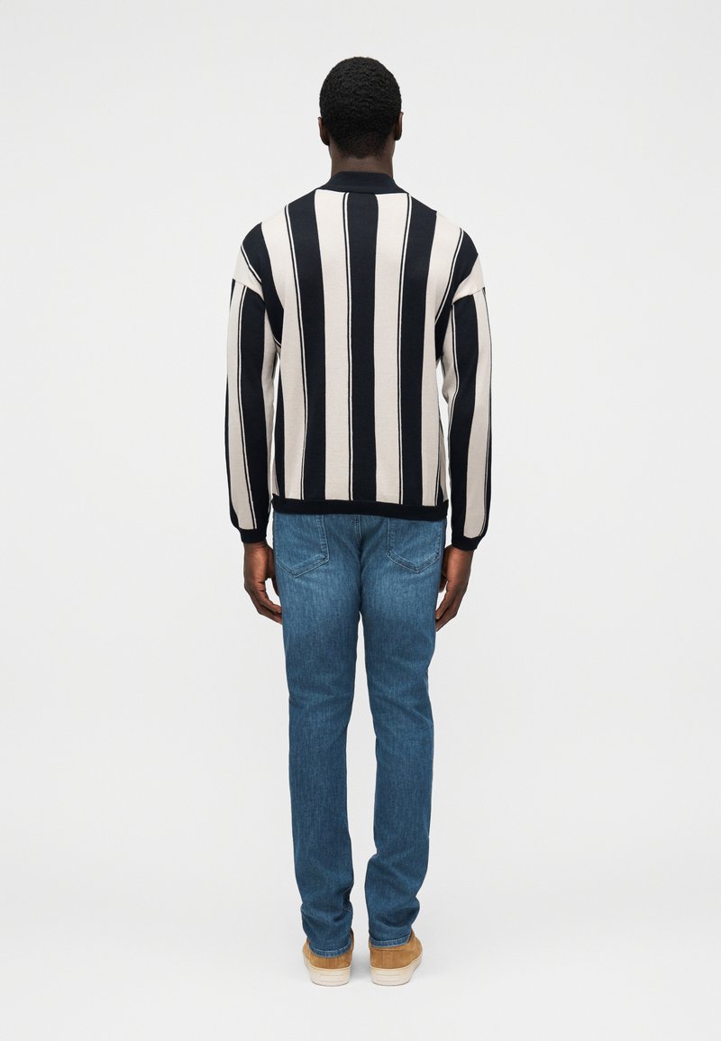 Pull rayé crème et marine, avec un col rond et des épaules tombantes, associé à un jean bleu clair et des baskets beige.