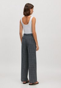 Zijde-brede broek met een marineblauw en wit geweven patroon, hoge taille en een gestructureerde afwerking. Gecombineerd met een witte top met ronde hals.