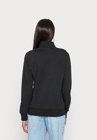 Sudadera negra con cuello alto, mangas largas y puños acanalados. Textura suave y diseño ajustado. Combinada con jeans de mezclilla azul claro.