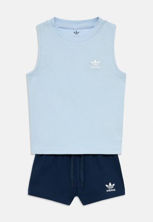 Svetlo modra brezrokavnik Adidas z majhnim logotipom, kombinirana z mornarsko modrimi Adidas kratkimi hlačami s pasom na vrvico in logotipom na levi nogi.