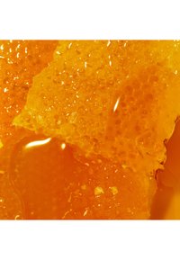 Tekstura plastra miodu wyeksponowana z złocistym bursztynowym miodem. Powierzchnia jest błyszcząca, z heksagonalnymi komórkami i lepkim, gęstym wyglądem.