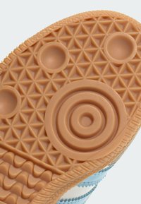 Hnedá gumová podrážka s textúrovanými geometrickými vzormi, vrátane špirály a kruhových detailov, a svetlomodrého bočného akcentu.