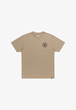 Béžové bavlněné tričko s malým černým kruhovým logem na levé části hrudníku. Standardní kulatý výstřih a krátké rukávy. Hladká textura.