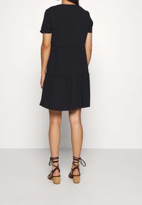 Black short-sleeve tiered dress with a round neckline, flowing fabric, and a loose fit. Worn with brown strappy high-heeled sandals.