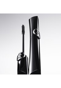 Svart mascararör med en kurvad design och metalliska detaljer, med en borste placerad bredvid. Slät, glänsande yta.