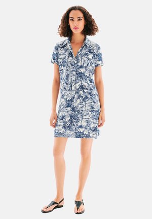 Robe à manches courtes bleue et blanche avec un motif de feuilles tropicales, boutonnière à l'avant et coupe classique, associée à des sandales plates noires.