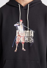 Black hoodie with a front graphic featuring a character from One Piece, detailed with bright colors, a sword, and "PUMA ONE PIECE" text.