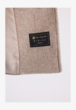 Beżowy płaszcz wełniany z teksturowanym, nakrapianym wzorem. Wyposażony w czarną metkę ze złotym napisem "Wool Collection" oraz "Makalu, wyprodukowano w Polsce."