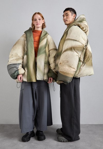 Padded jackets in earthy tones with unique textured patterns. Model pairs with loose gray pants and chunky black footwear.
