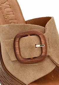 Sandalia deslizante de ante beige con una tira ancha y una gran hebilla de madera, plantilla de color marrón texturizado en contraste y forro de cuero suave.