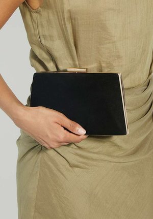 Zwarte fluwelen clutch met gouden accenten, rechthoekige vorm, gladde textuur, vastgehouden tegen een persoon in een groene outfit.