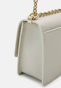 Gestuctureerde beige leren handtas met een gestructureerde afwerking, voorzien van een gouden kettingriem en gestikte accenten langs de randen.