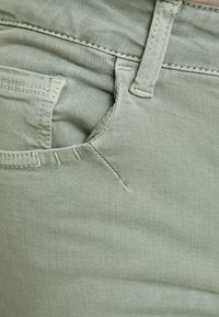 Tejido de mezclilla verde claro de pantalones con un bolsillo frontal que destaca por las costuras visibles y la textura, enfatizando la durabilidad y los detalles de diseño.