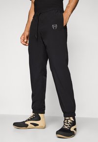 Black jogger pants with elastic waistband, side pockets, and a white snake logo. Features elastic cuffs and a lightweight, smooth texture.