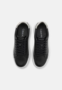 Černé kožené tenisky s bílými gumovými podrážkami, šněrovací design, polstrovaný límec a decentní značení na vnitřní straně. Hladký povrch.