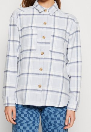 Camicia a quadri bianca e blu con colletto, bottoni in legno e due tasche sul petto. Tessuto testurizzato, vestibilità comoda.