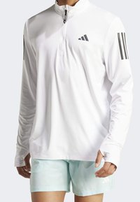 Biała koszula z długim rękawem z kołnierzem na pół-zamek i czarnym logo adidas, w zestawie z szortami w miętowym kolorze, zaprojektowana z myślą o odzieży sportowej.