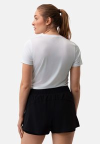 Vit idrottströja i kombination med svarta shorts. Tröjan har en slät yta och korta ärmar, medan shortsen har ett elastiskt midjeband.