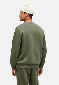 Groene sweatshirt met een relaxed fit, geribde boorden en zoom, gemaakt van zachte stof. Een crèmekleurige beanie met groene letters maakt de look compleet.