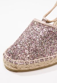 Espadrille scintillante avec un dessus en matériau pailleté rose et argent, semelle en corde naturelle et des détails de bord cousus.