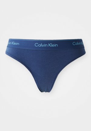 Tumši zils kokvilnas tanga ar atbilstošu elastīgu jostasvietu, kurā ir gaismas zilā krāsā „Calvin Klein” logo. Gluda tekstūra un izsmalcināts dizains.