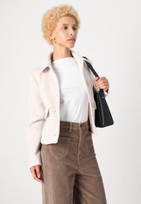 Lichtroze visgraatjack met twee knopen, gedragen over een witte blouse en een paarse corduroy broek, gecombineerd met een zwarte handtas.