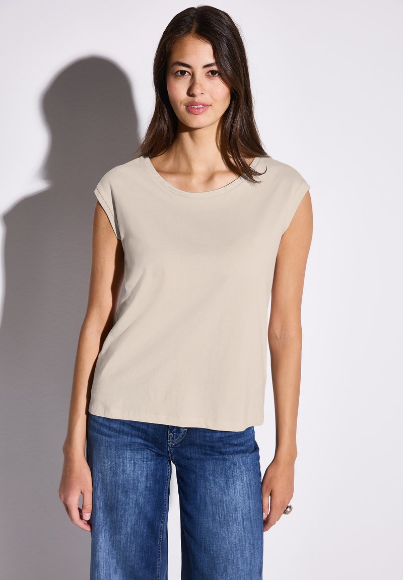 Beige t-shirt med kort ärm och rund halsringning, tillverkad av mjukt tyg, i kombination med blå denim jeans med vida ben. Enkelt design och slät textur.