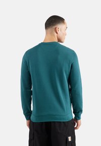 Sudadera de cuello redondo en color verde azulado, hecha de tela suave, con mangas largas y puños acanalados. La vista trasera resalta la textura suave y el diseño sencillo.