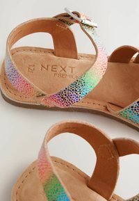Flat sandals with a rainbow-hued perforated synthetic upper, tan leather insole, and a silver buckle accent on a round ankle strap.
