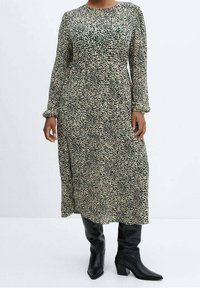 Robe vert à manches longues avec un motif floral en crème et vert foncé ; a un col rond et tombe sous le genou, assortie à des bottes noires jusqu'au genou.