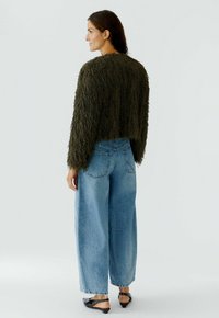 Green shaggy cropped jacket with long sleeves, paired with light blue wide-leg jeans and black slip-on shoes. Minimalist background.