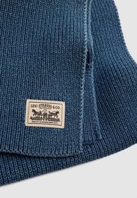 Tecido de malha canelada azul com textura tecida, apresentando uma etiqueta de marca com a inscrição "Levi Strauss & Co." costurada na borda.