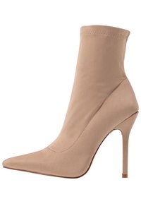 Botín de tacón alto color beige con punta afilada, tacón stiletto delgado y parte superior de tela suave que se extiende por encima del tobillo.