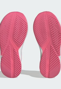 Scarpe sportive bianche con suole in gomma rosa, caratterizzate da un motivo testurizzato e scanalature angolate per trazione e stabilità.