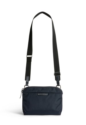 Sac bandoulière compact noir avec sangle large réglable et fermeture éclair, design minimaliste avec logo de marque discret sur le devant.