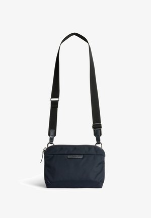 Sac bandoulière compact noir avec sangle large réglable et fermeture éclair, design minimaliste avec logo de marque discret sur le devant.