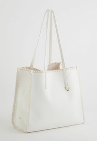 Sac fourre-tout synthétique blanc avec une finition texturée, des coutures crème, une forme structurée et de longues poignées. Présente un accent en matériau doré.