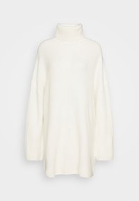 Vit polotröja i strukturerad stickad kvalitet med sänkta axlar och sidospalt för ökad rörelsefrihet.