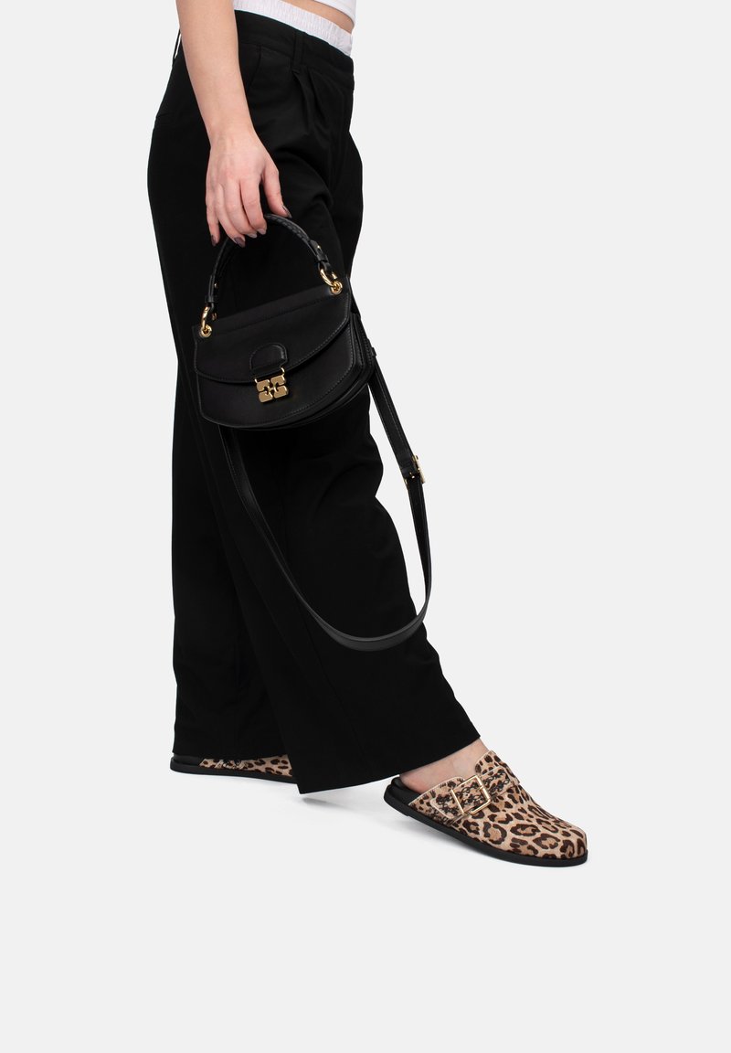 Leopardenmuster Slipper mit flacher Sohle, kombiniert mit lockeren schwarzen Hosen und einer kleinen schwarzen Handtasche mit goldenen Beschlägen.