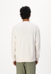 Lys beige langermet genser med teksturert strikk, rund hals og ribbede mansjetter. Minimalistisk design, ingen synlige logoer eller mønstre.