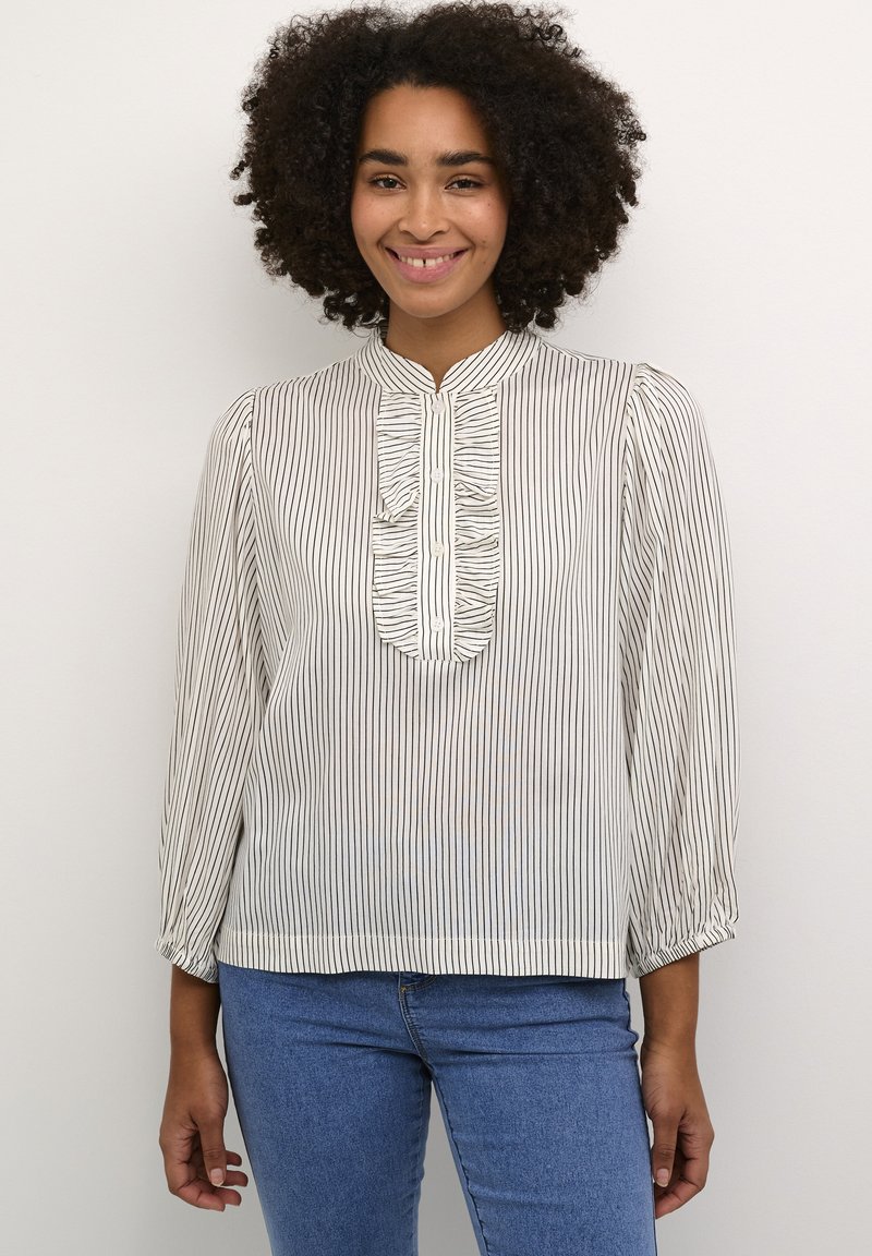 Blusa blanca con rayas verticales negras, con un pliegue con volante y cierre de botones, mangas tres cuartos y un corte holgado.