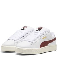 Sneaker bianche in pelle sintetica con una striscia laterale bordeaux, punta tonda e suola in gomma color crema con texture e un motivo di battistrada spesso.