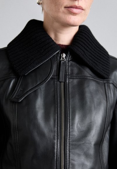 Black leather jacket featuring a ribbed black collar, front zipper closure, and smooth texture. Notable stitching along the seams.