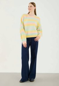 Gestreifter Pullover in Pastellfarben Gelb, Pink und Hellblau, kombiniert mit marineblauen Hosen mit weitem Bein. Der Pullover hat einen Rundhalsausschnitt und eine mittlere Strickstruktur.