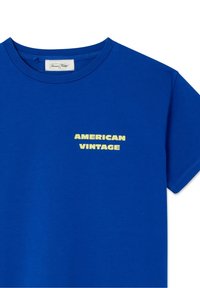 Modra bombažna majica s kratkimi rokavi. Na levi strani prsnega predela je natisnjen napis "AMERICAN VINTAGE" v rumeni barvi. Okrogel izrez, enobarvna.