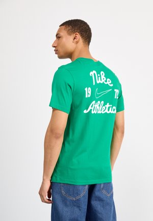 T-shirt verde in cotone con testo bianco "Nike" e "Athletics" e un piccolo logo, scollo rotondo e maniche corte. Vestibilità casual.