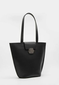 Borsa tote nera realizzata in materiale liscio con una forma trapezoidale, dotata di chiusura a patta e di un accento metallico esagonale. Manici lunghi e piatti.