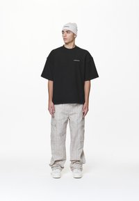 T-shirt nera oversize a maniche corte, con un piccolo logo; abbinata a pantaloni cargo grigio chiaro e sneakers bianche.