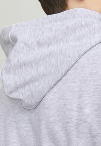 Grijze hoodie van een zachte, gestructureerde stof. Heeft een fitted capuchon en een iets losse pasvorm, met subtiele kleurvariaties.